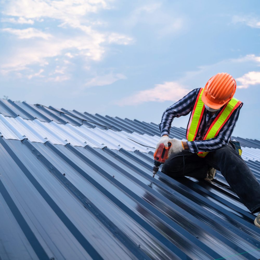 Asian Roofer worker safety wear using air or pneumatic nail gun Asian Roofer worker safety wear using air or pneumatic nail gun and installing on new roof metal sheet, Roof concept of residential building under construction.